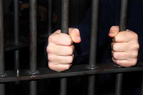 man holding bars from inside jail cell
